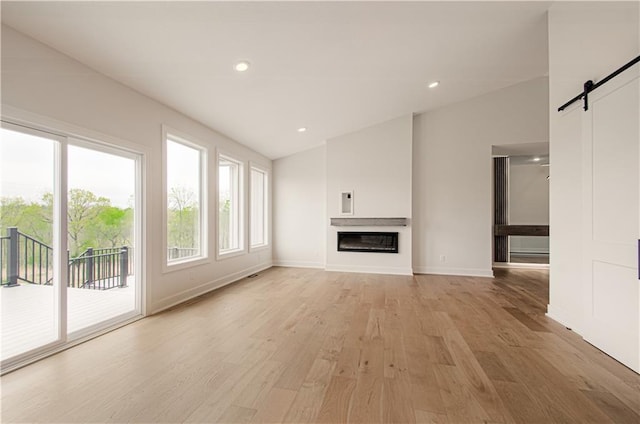 7551 NW Gower Ave, Kansas City, MO 64151 - unfurnished living room featuring light wood-style flooring, a barn door, baseboards, a glass covered fireplace, and vaulted ceiling