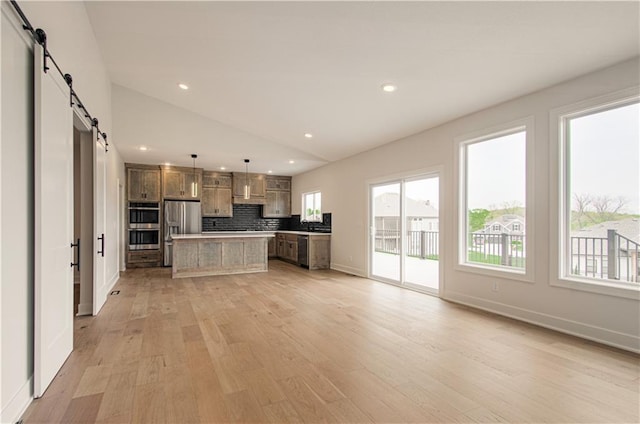 7551 NW Gower Ave, Kansas City, MO 64151 - kitchen with decorative backsplash, appliances with stainless steel finishes, a barn door, open floor plan, and light wood finished floors