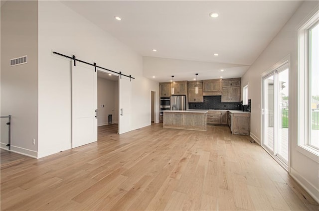 7551 NW Gower Ave, Kansas City, MO 64151 - unfurnished living room with light wood finished floors, a barn door, plenty of natural light, and visible vents