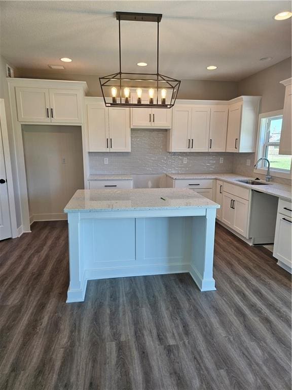 kitchen featuring light stone counters, pendant lighting, white cabinets, sink, and a center island