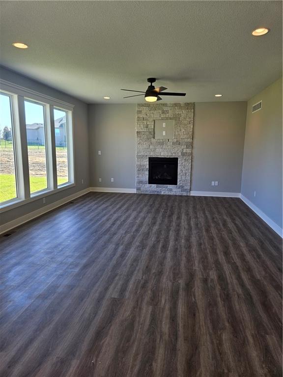 unfurnished living room featuring a textured ceiling, a fireplace, dark hardwood / wood-style floors, and ceiling fan