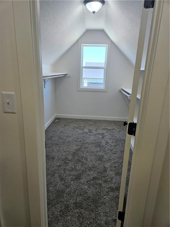 bonus room with a textured ceiling, lofted ceiling, and dark colored carpet