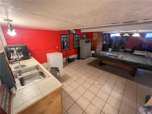 kitchen featuring sink, a textured ceiling, tile counters, light tile patterned flooring, and brick wall