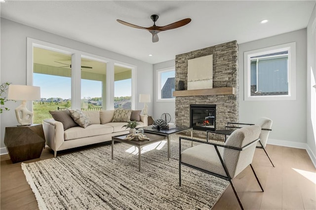 living room featuring hardwood / wood-style floors, a stone fireplace, and ceiling fan