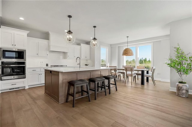 kitchen featuring light hardwood / wood-style floors, stainless steel appliances, pendant lighting, and white cabinets