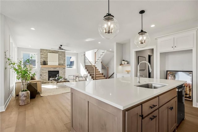 kitchen featuring a center island with sink, white cabinetry, light hardwood / wood-style flooring, a stone fireplace, and sink