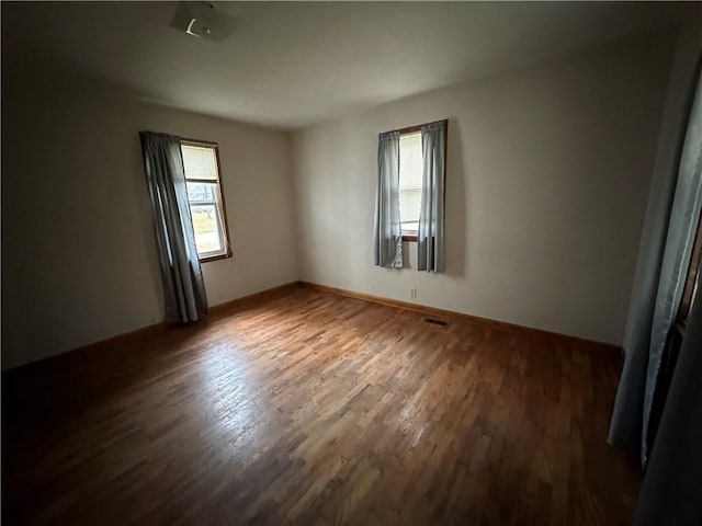 empty room featuring a wealth of natural light, visible vents, dark wood finished floors, and baseboards