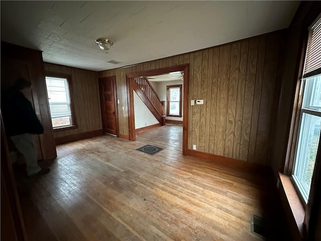 spare room with wood walls, wood finished floors, visible vents, baseboards, and stairs