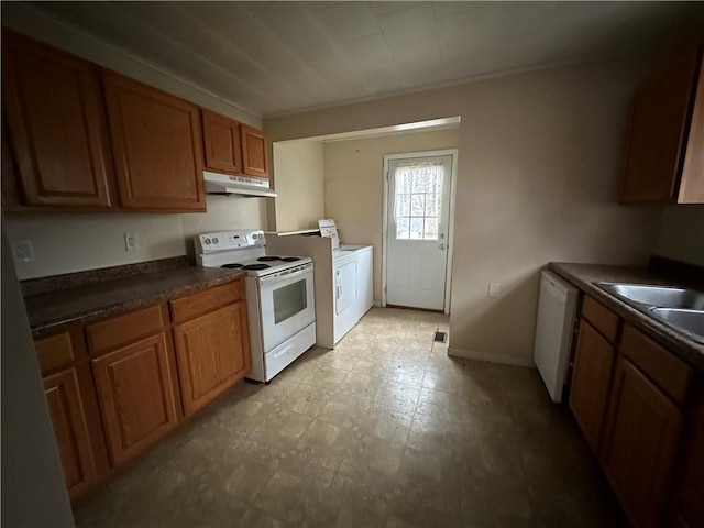 kitchen with under cabinet range hood, white appliances, brown cabinetry, dark countertops, and washer / dryer