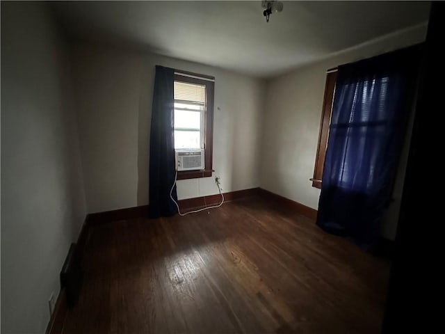 empty room featuring cooling unit, dark wood-style flooring, and baseboards