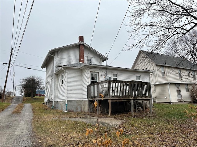 rear view of property with a deck, driveway, and a chimney