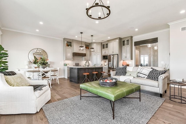 living room featuring light hardwood / wood-style flooring, sink, a chandelier, and crown molding