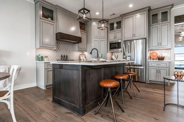 kitchen featuring built in microwave, a kitchen island with sink, gray cabinetry, stainless steel fridge with ice dispenser, and custom exhaust hood