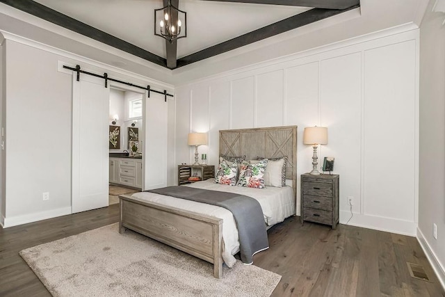 bedroom featuring an inviting chandelier, dark hardwood / wood-style floors, ensuite bath, and a barn door