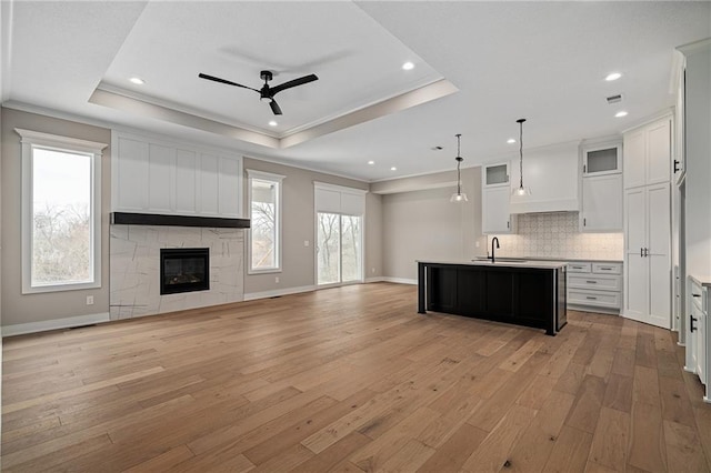 kitchen with plenty of natural light, a tray ceiling, white cabinets, hanging light fixtures, and a kitchen island with sink