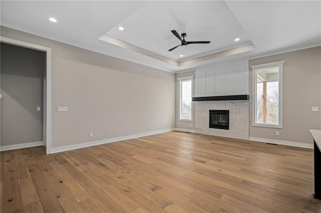 unfurnished living room with light wood-type flooring, a tile fireplace, ceiling fan, and a raised ceiling