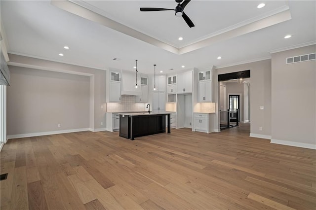 unfurnished living room with sink, light hardwood / wood-style flooring, ceiling fan, and a raised ceiling