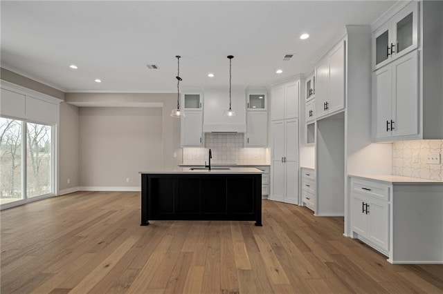 kitchen featuring a center island with sink, decorative light fixtures, light wood-type flooring, and white cabinets