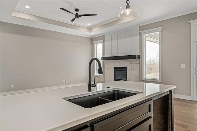 kitchen with a raised ceiling, white cabinetry, sink, and pendant lighting