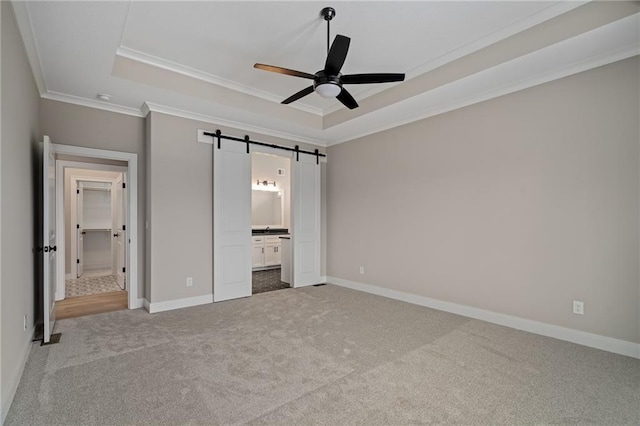 unfurnished bedroom featuring a barn door, crown molding, carpet, and a raised ceiling