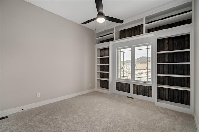 spare room featuring light carpet, ceiling fan, and built in shelves