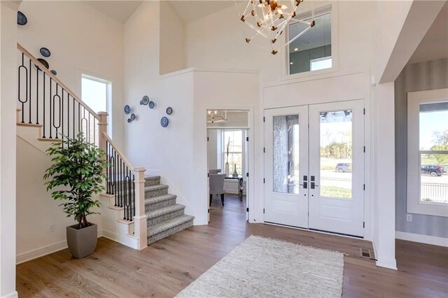 entryway with a towering ceiling, french doors, hardwood / wood-style floors, and an inviting chandelier