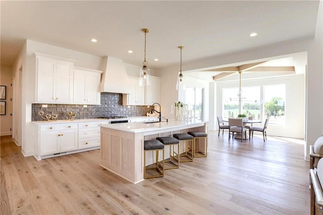 kitchen featuring light hardwood / wood-style flooring, an island with sink, premium range hood, and white cabinetry