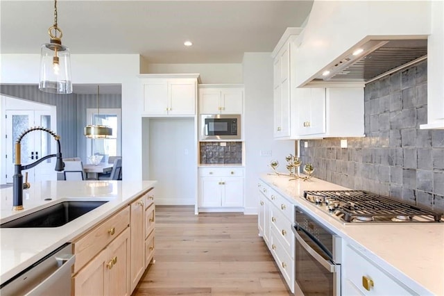 kitchen with light hardwood / wood-style flooring, pendant lighting, backsplash, stainless steel appliances, and sink