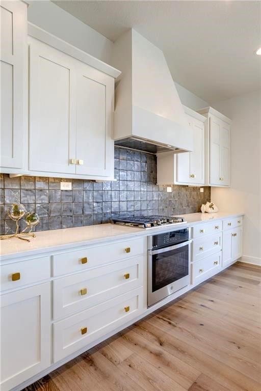 2461 W 176th St, Overland Park, KS 66085 - kitchen featuring light wood-type flooring, premium range hood, white cabinetry, decorative backsplash, and stainless steel appliances