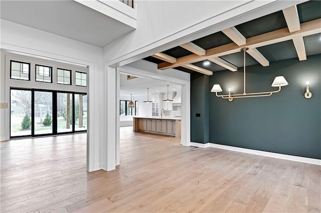 interior space with beamed ceiling, an inviting chandelier, sink, and light hardwood / wood-style flooring