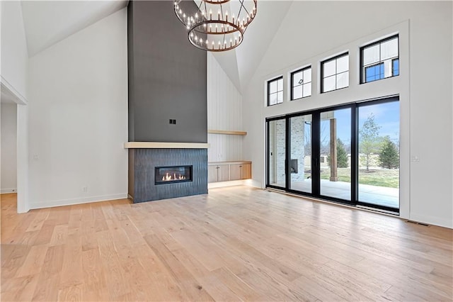 unfurnished living room featuring a large fireplace, a chandelier, high vaulted ceiling, and light hardwood / wood-style flooring