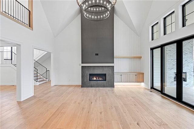 unfurnished living room featuring light hardwood / wood-style flooring, high vaulted ceiling, and a chandelier