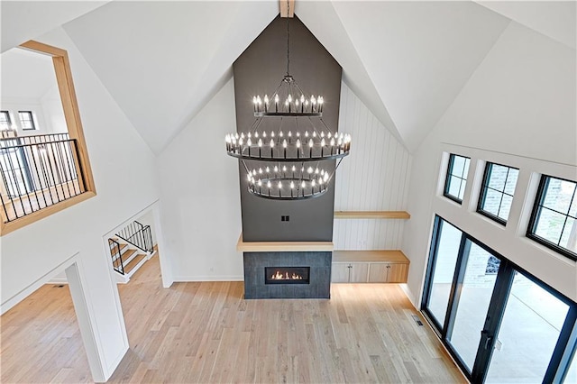 unfurnished living room with a tiled fireplace, high vaulted ceiling, light wood-type flooring, and an inviting chandelier