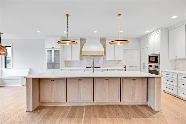 kitchen with a large island with sink, custom exhaust hood, and oven