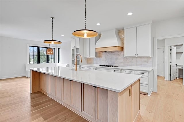 kitchen with a large island with sink, white cabinetry, custom range hood, and stainless steel gas stovetop