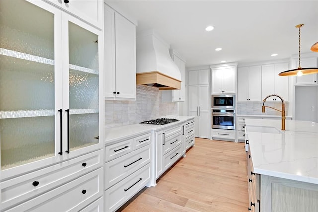 kitchen with premium range hood, decorative light fixtures, light wood-type flooring, stainless steel appliances, and white cabinets