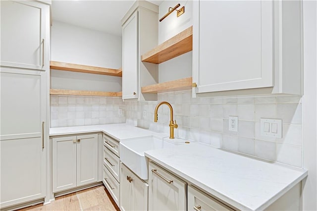 kitchen featuring white cabinetry, light stone countertops, sink, and backsplash