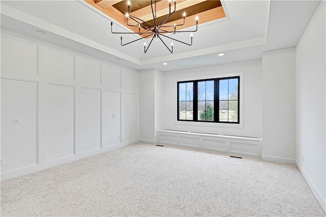 carpeted empty room with a raised ceiling and a chandelier