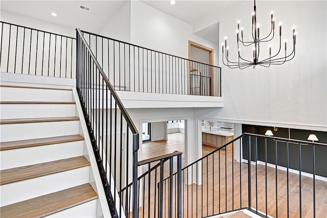 staircase with a high ceiling, wood-type flooring, and a chandelier