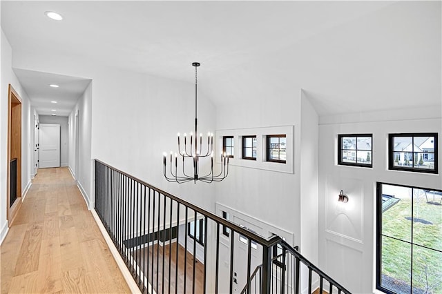 hallway with light hardwood / wood-style flooring, a chandelier, and vaulted ceiling