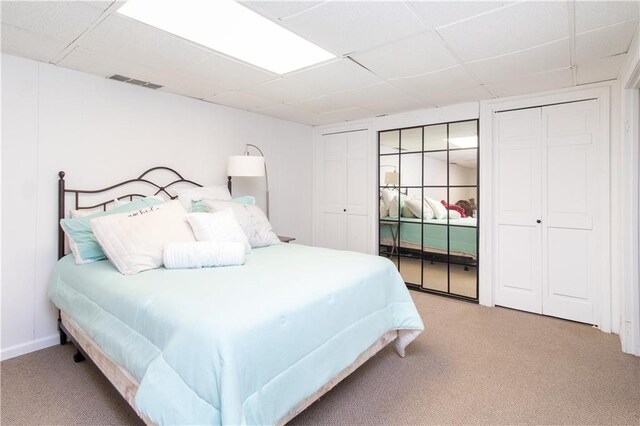 bedroom with a paneled ceiling, light colored carpet, and multiple closets