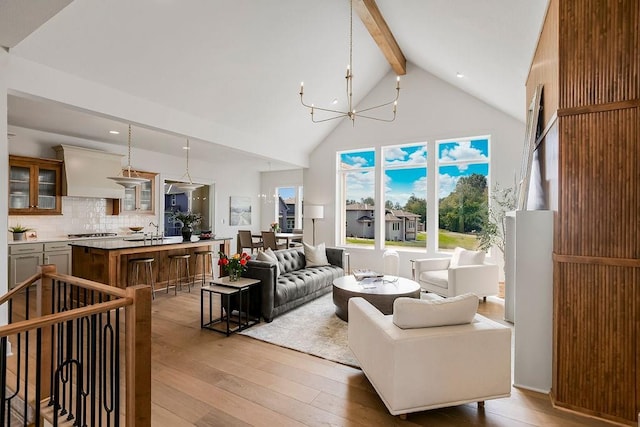 living room featuring sink, high vaulted ceiling, light wood-type flooring, a notable chandelier, and beamed ceiling