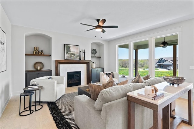 living room featuring a fireplace, ceiling fan, light wood-type flooring, and built in features