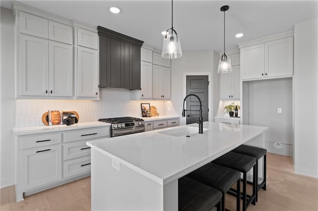 kitchen featuring an island with sink, tasteful backsplash, light wood-type flooring, and stainless steel gas range oven