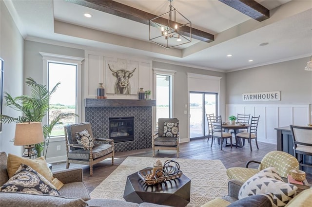 living room with dark wood-type flooring, an inviting chandelier, crown molding, beamed ceiling, and a tiled fireplace