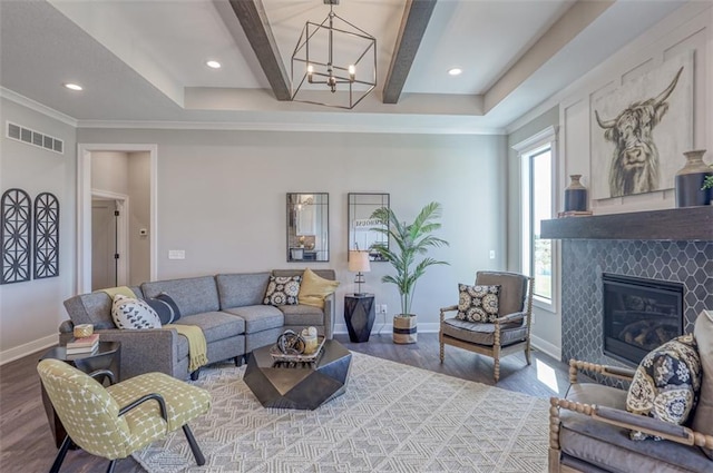 living room featuring hardwood / wood-style floors, a tile fireplace, an inviting chandelier, crown molding, and beamed ceiling