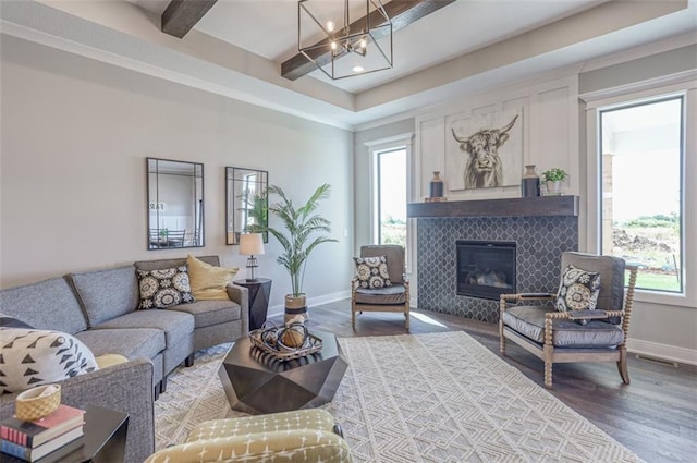 living room featuring beamed ceiling, wood-type flooring, a tile fireplace, and a chandelier