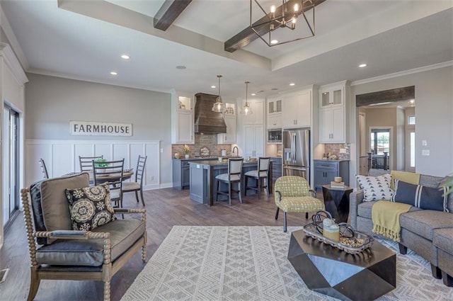 living room featuring ornamental molding, sink, beam ceiling, wood-type flooring, and a chandelier