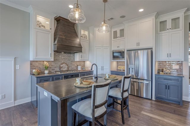 kitchen featuring blue cabinets, premium range hood, a kitchen island with sink, white cabinets, and appliances with stainless steel finishes