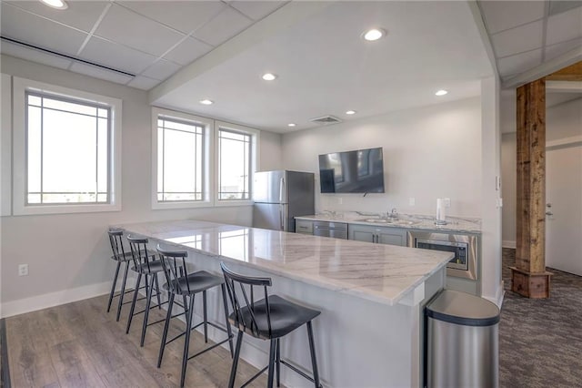 kitchen with a kitchen bar, appliances with stainless steel finishes, kitchen peninsula, light stone counters, and sink